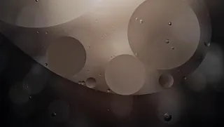 Abstrakt bilde av store og små oljedråper i vann med mørk, dempet belysning.